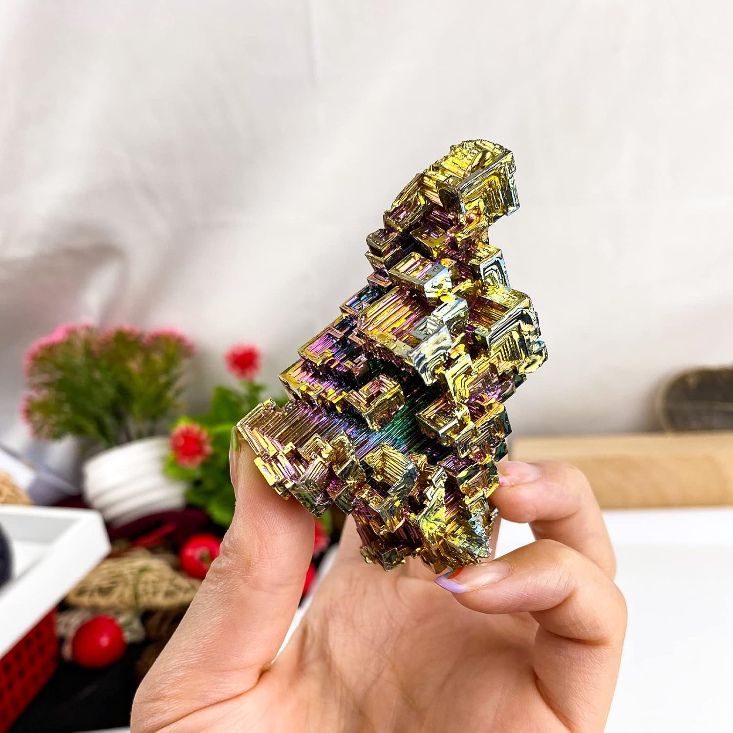 Lab-grown Bismuth Crystal Cluster

A striking iridescent bismuth crystal specimen displaying geometric, stacked rectangular formations in shimmering gold, purple, and rainbow hues, held in a hand against a soft-focus background with potted flowers.