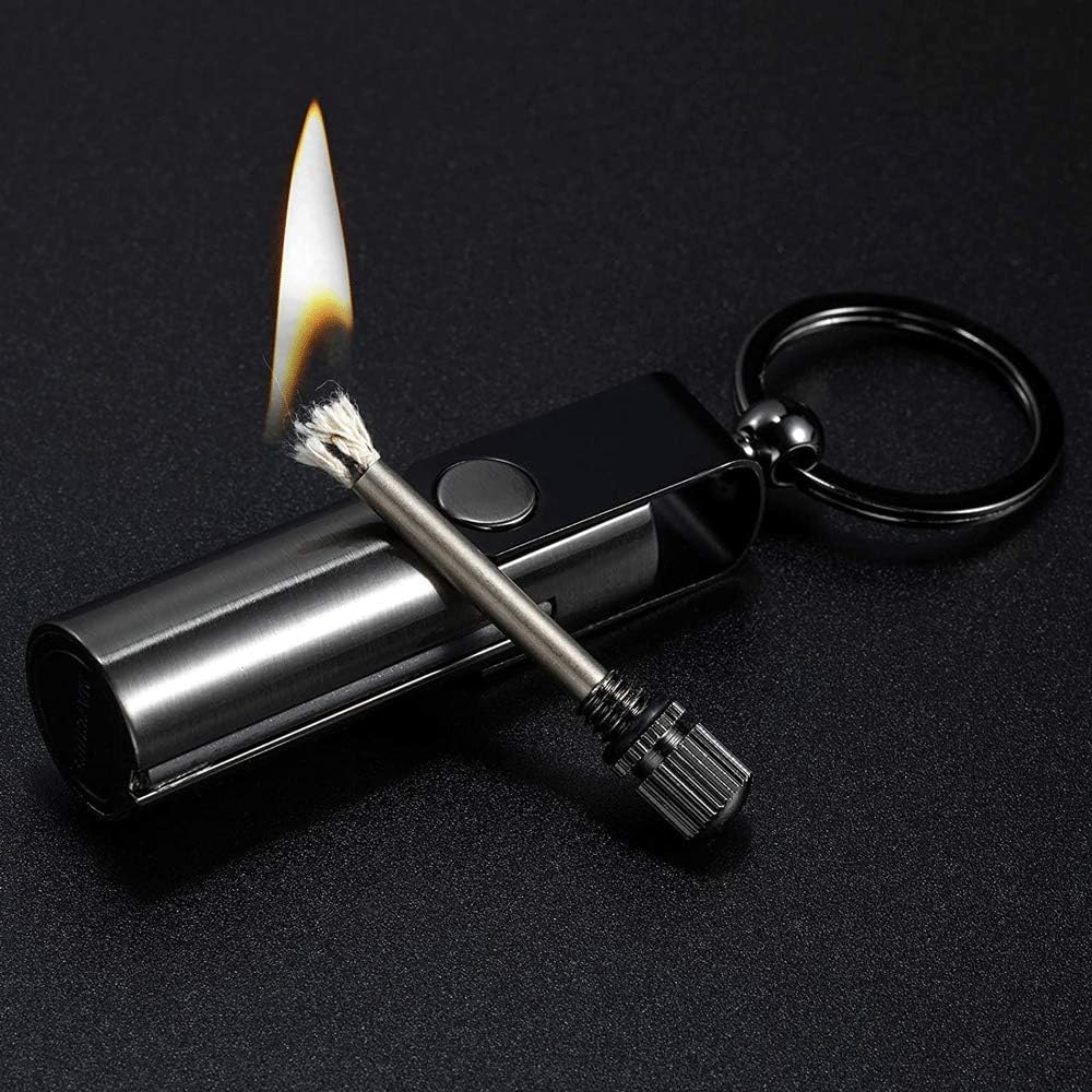 A compact metallic permanent match survival keychain with a lit flame, featuring a cylindrical metal body, attached key ring, and a brush-like match head that produces a sustained flame.